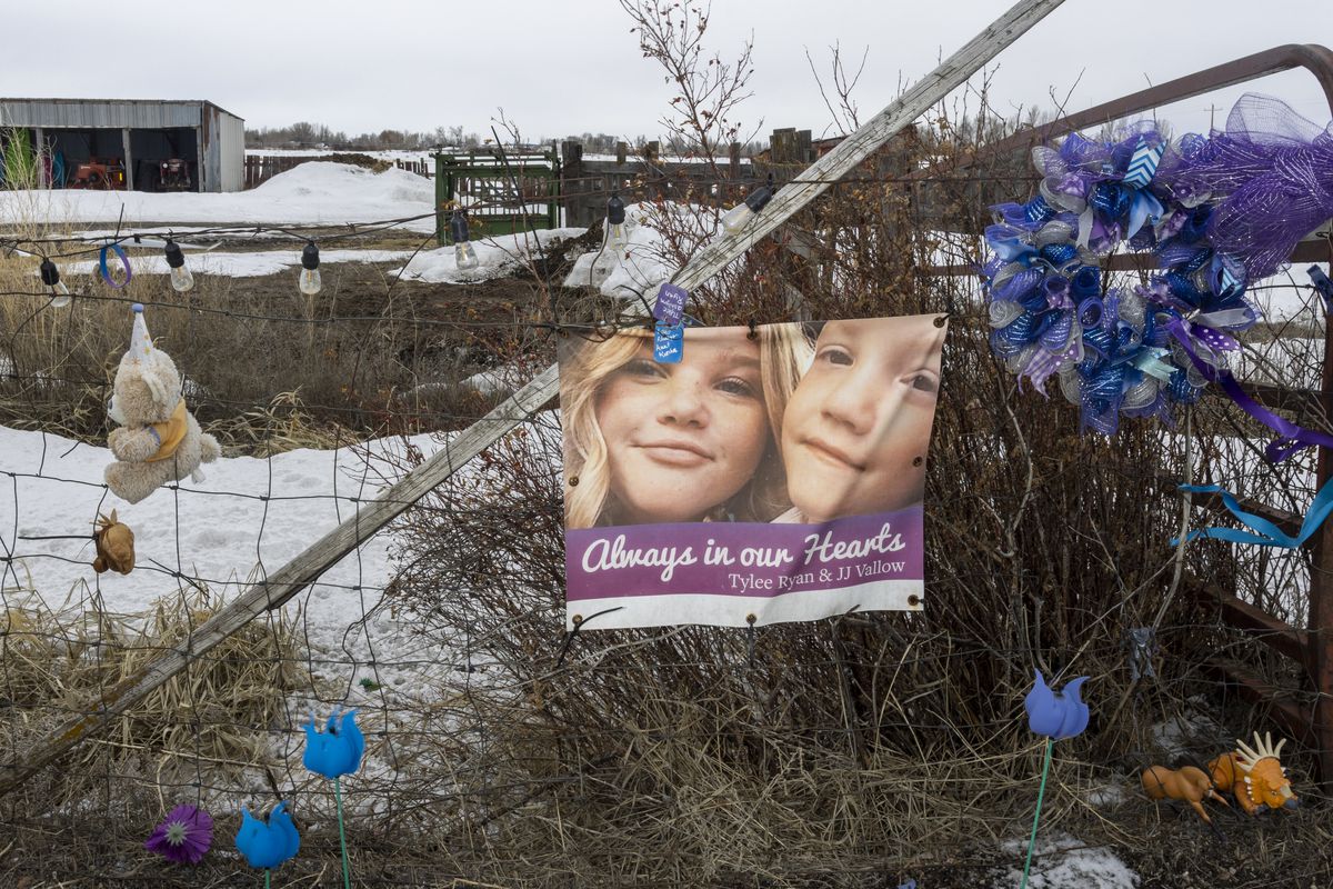 A banner featuring two smiling children hanging on a wire fence in a rural snowy scene. Blue artificial flowers and a teddy bear also hang on the fence.