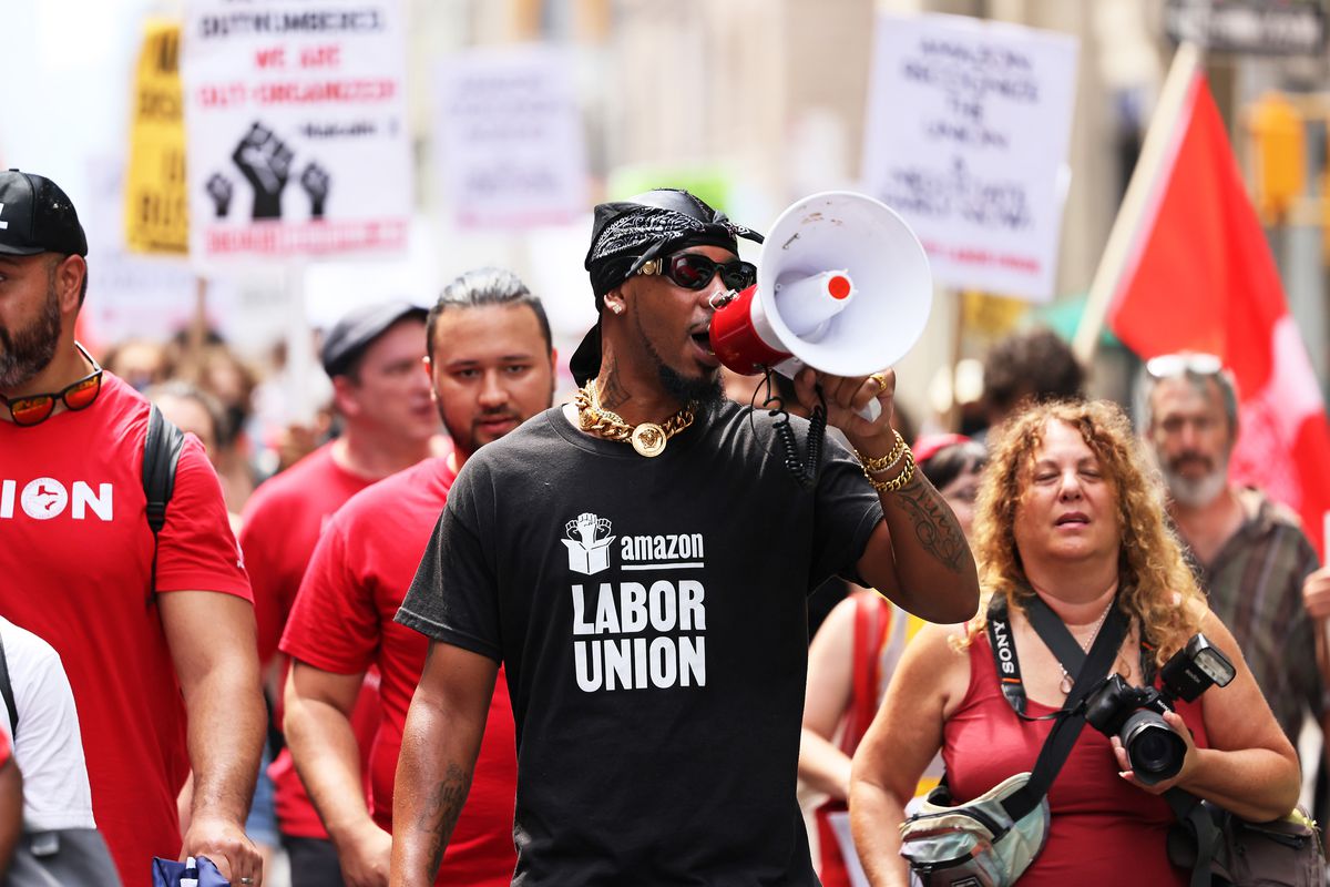 Christian Smalls speaks into a bullhorn at a protest. He’s wearing a shirt that says “Amazon Labor Union.”