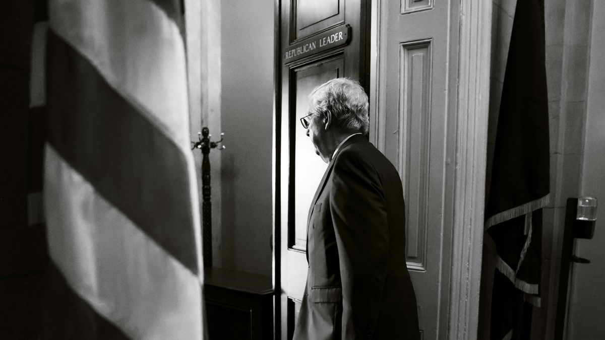 A black-and-white photograph of Mitch McConnell walking through a door away from the camera.