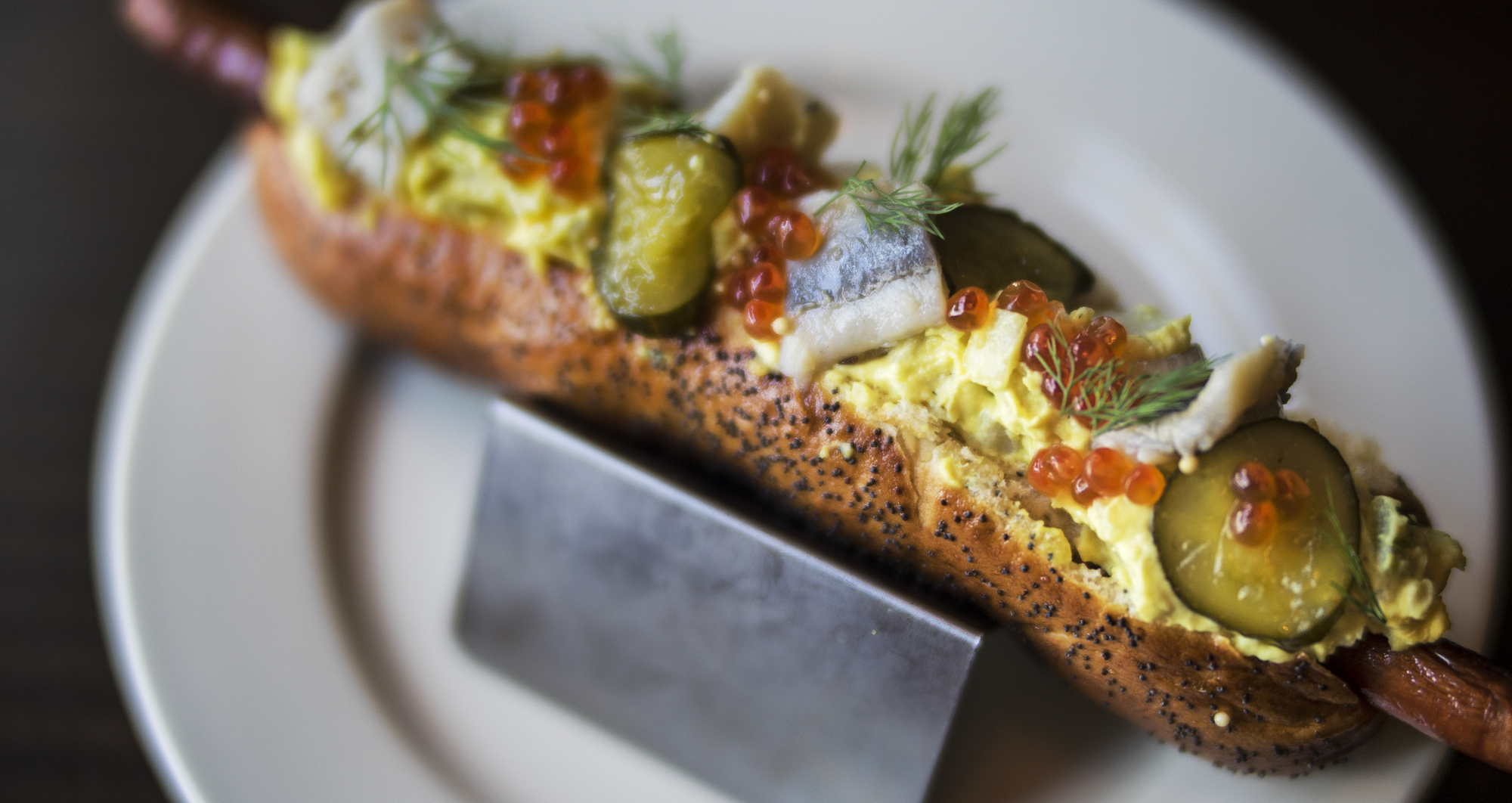 A foot-long hot dog is dressed with potato salad, pickled herring, fermented cucumber and salmon roe.