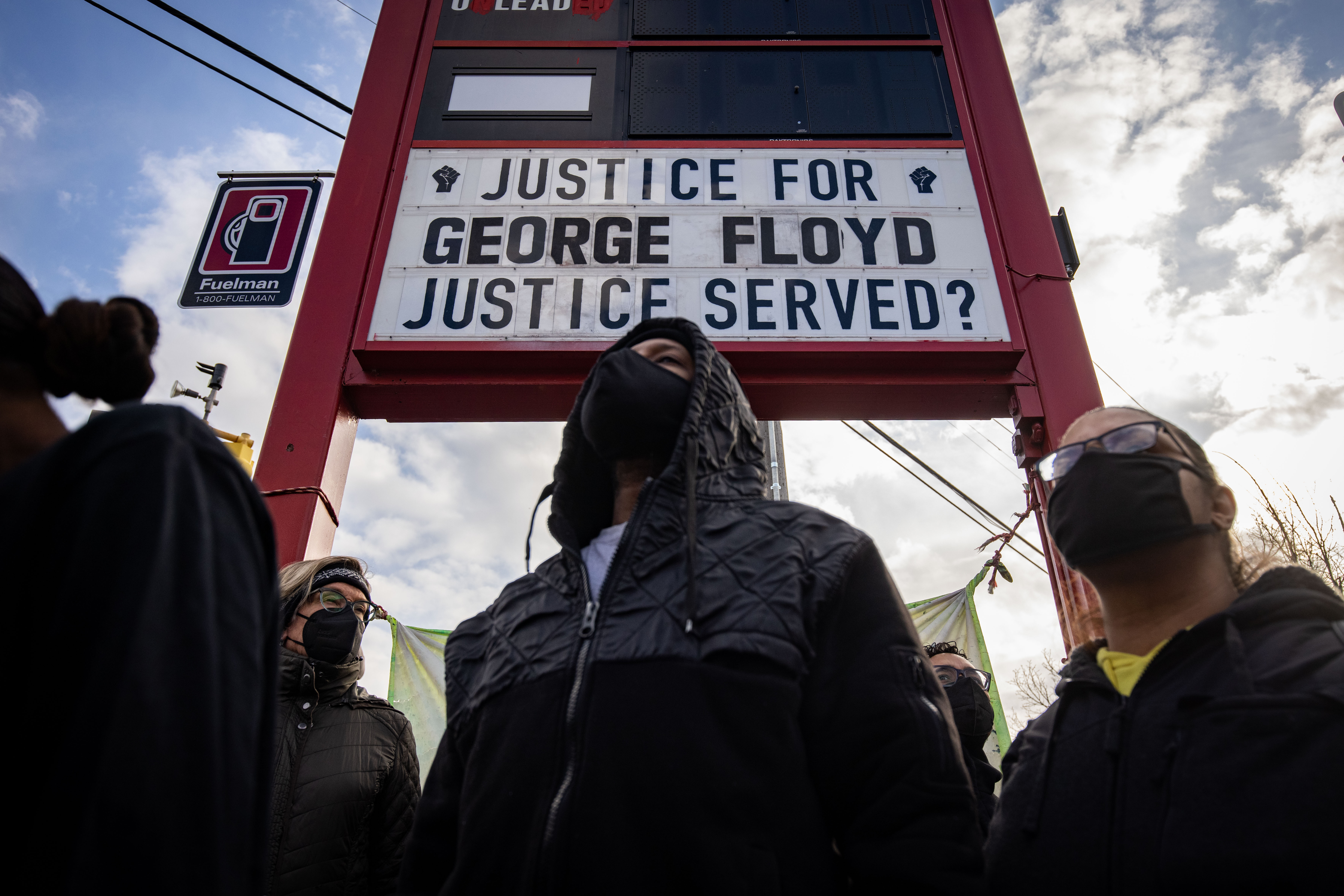 Black people in masks stand beneath a gas station sign; the area that would normally have the gas prices reads: “Justice for George Floyd;” underneath that is the message: “Justice served?”