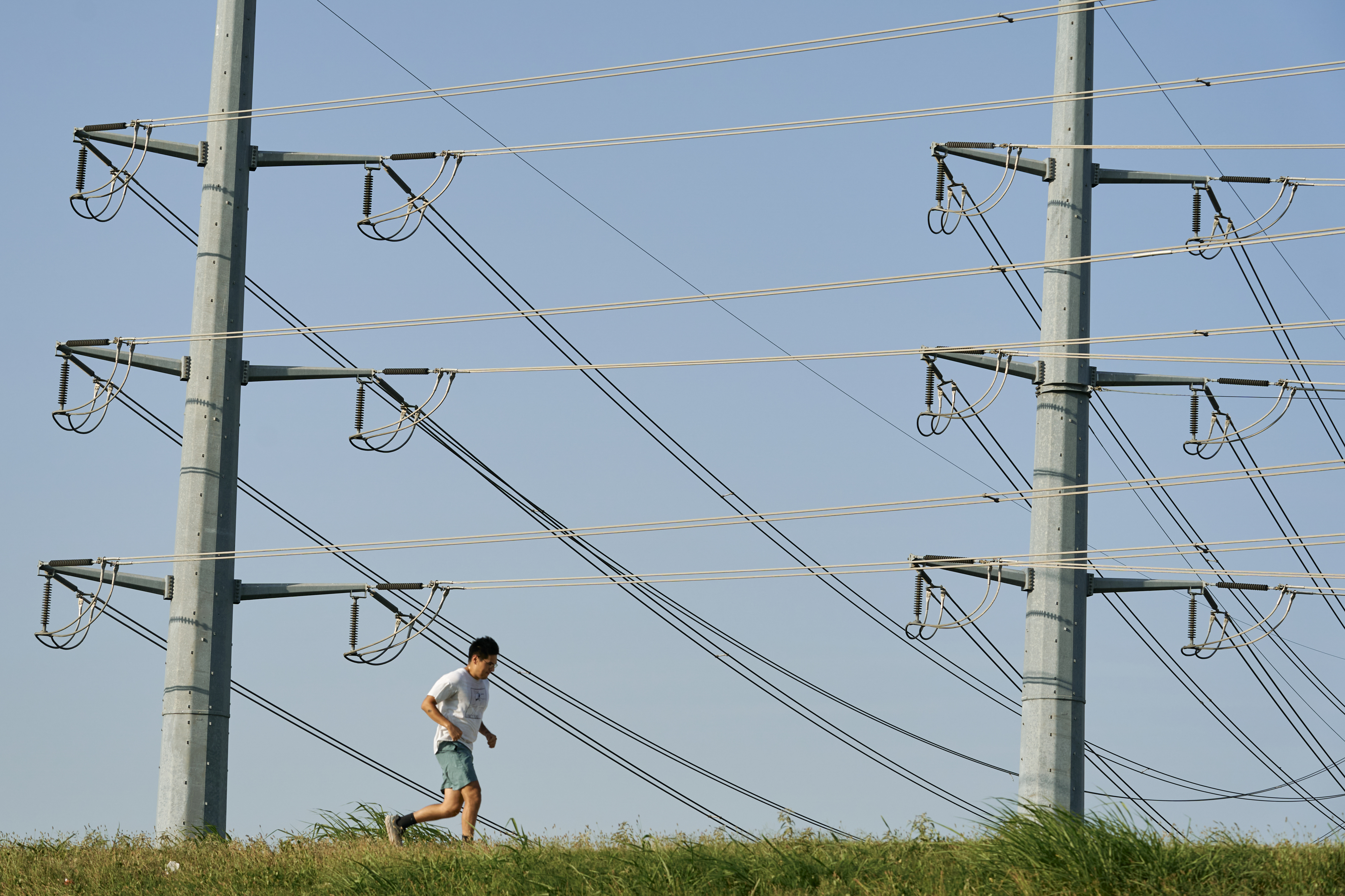 A jogger runs past large poles holding electric wires.