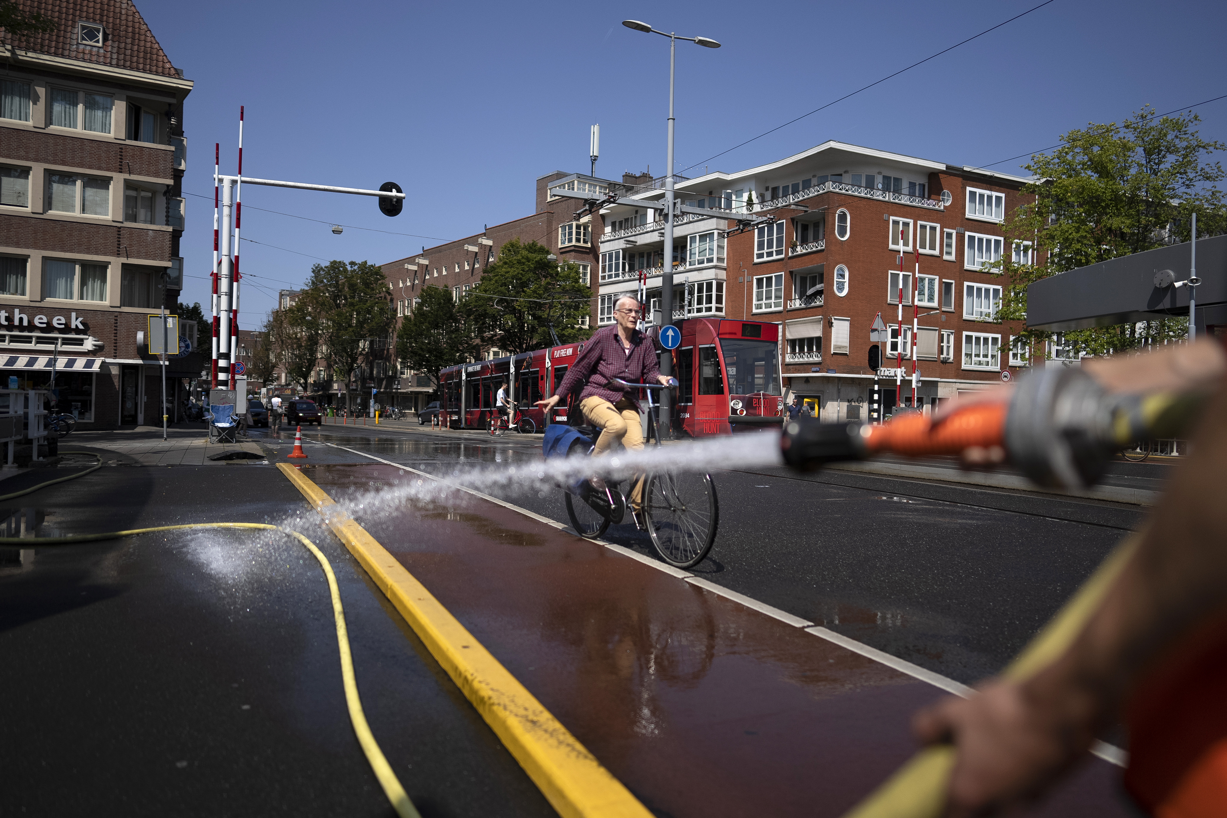 A bicyclist rides by a hose spraying water onto the road surface of a nearby bridge.