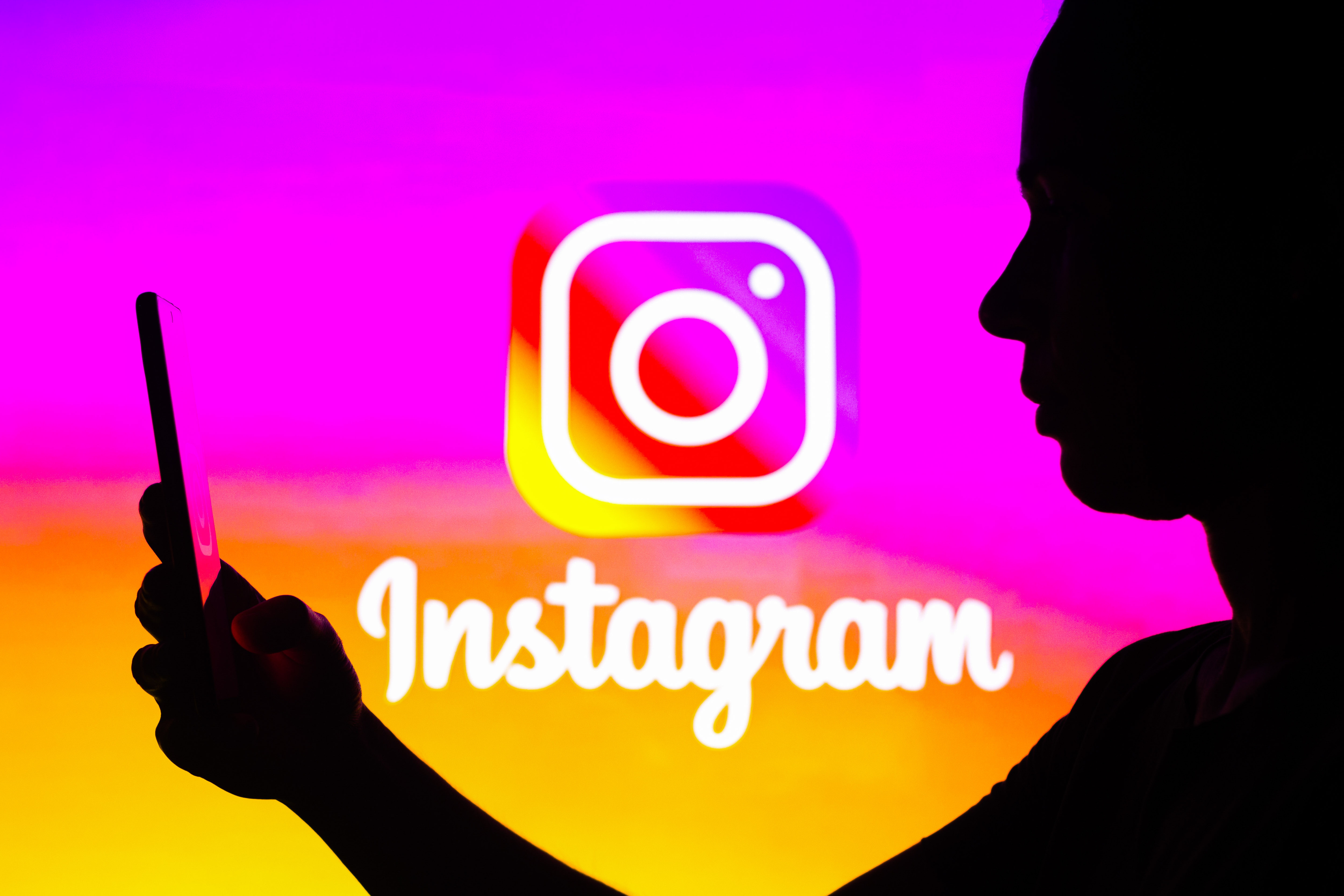 The instagram logo behind the silhouette of a person looking at their phone.
