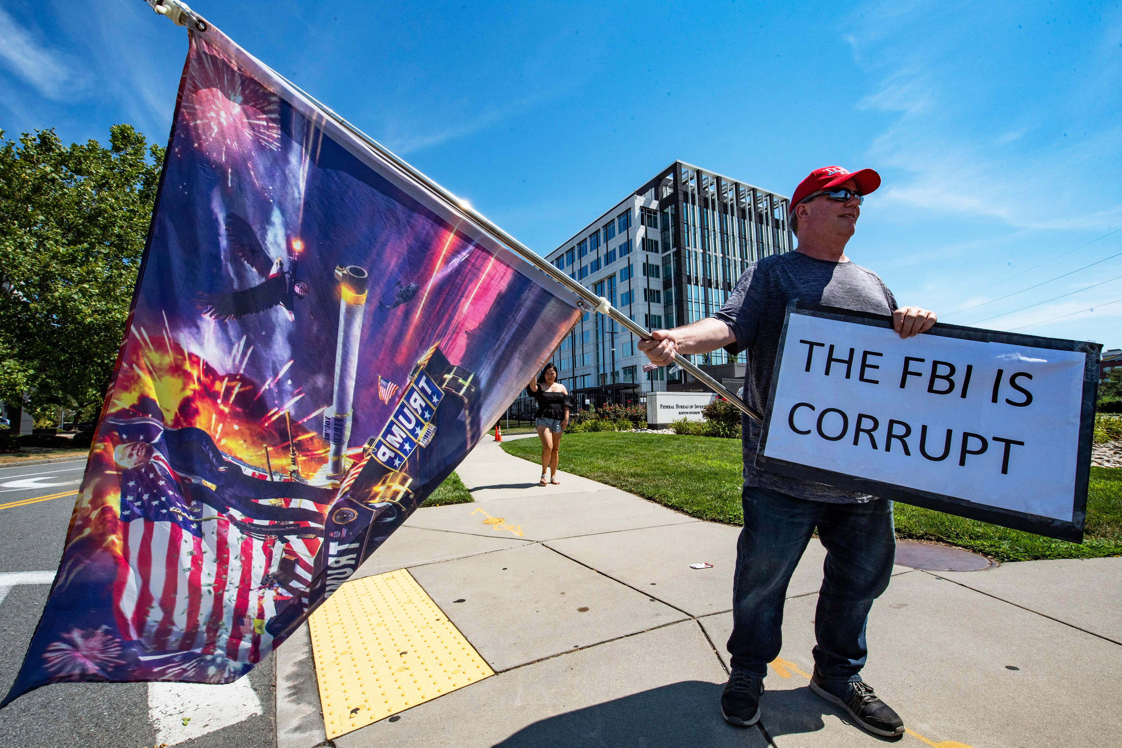 A demonstrator holding a flag and a sign that reads “The FBI is corrupt.”