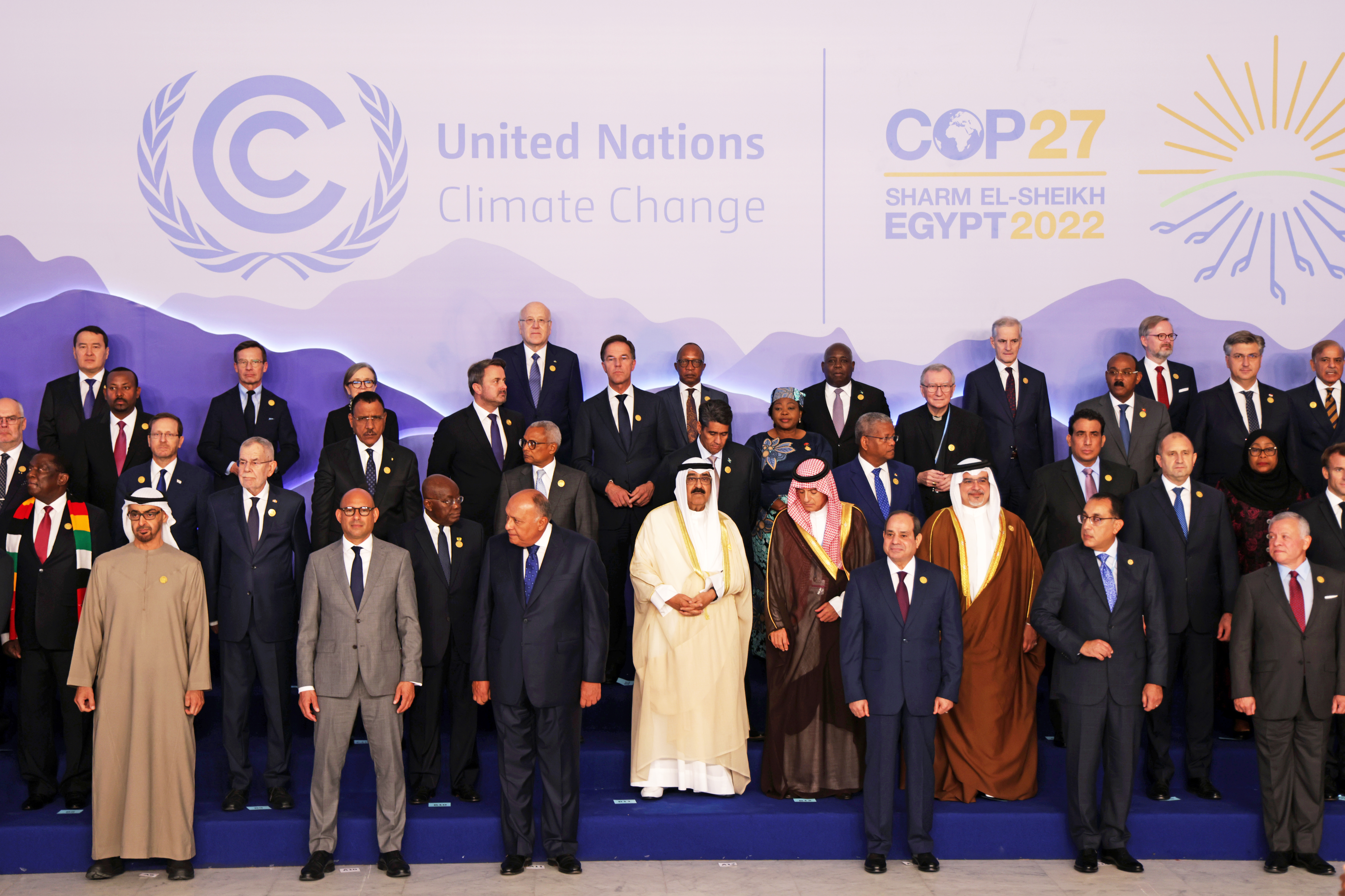A group photo of leaders from many countries standing against a purple COP27 background. 