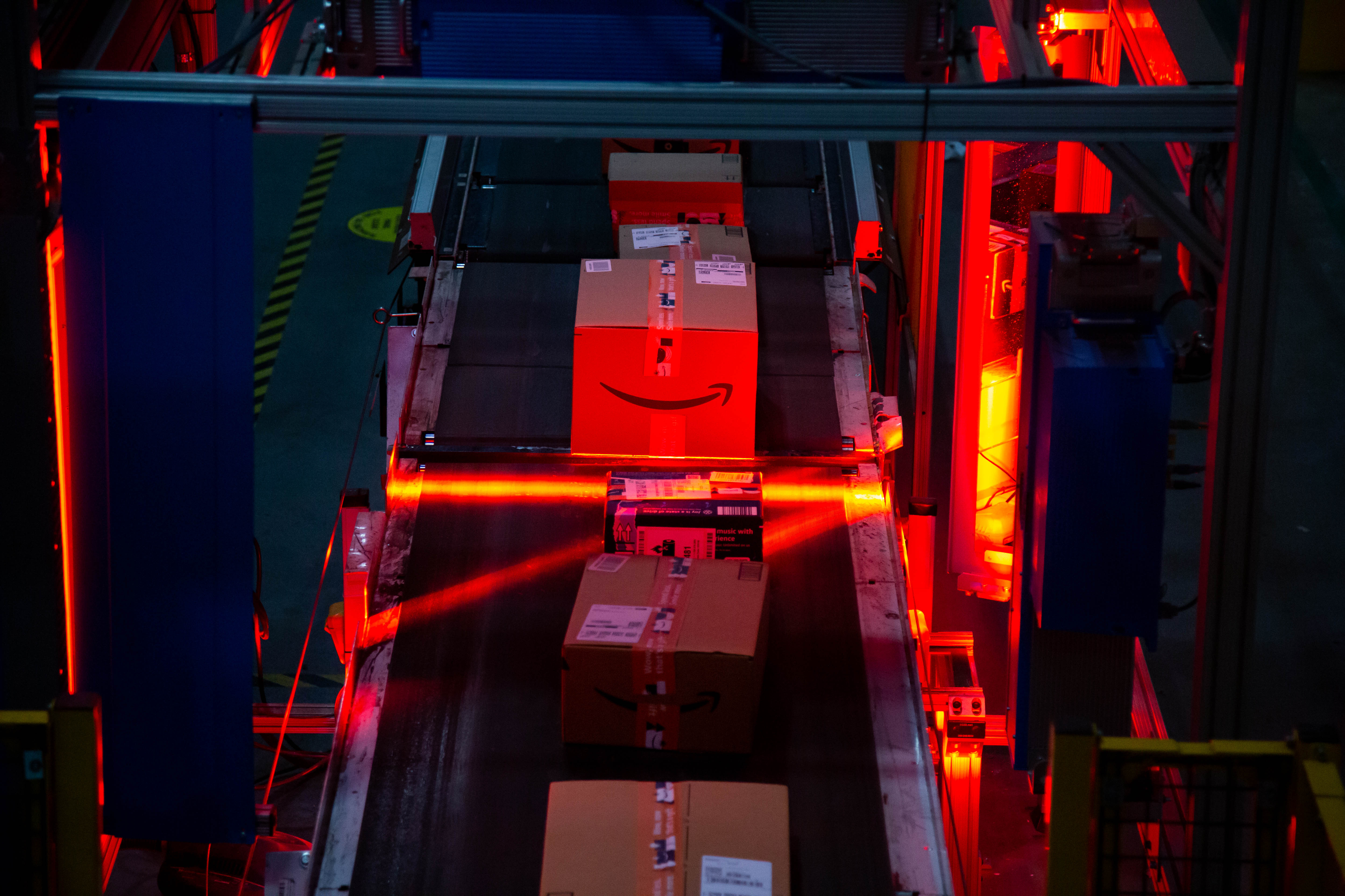 An Amazon-branded box moves through a red light scanner on a conveyer belt.