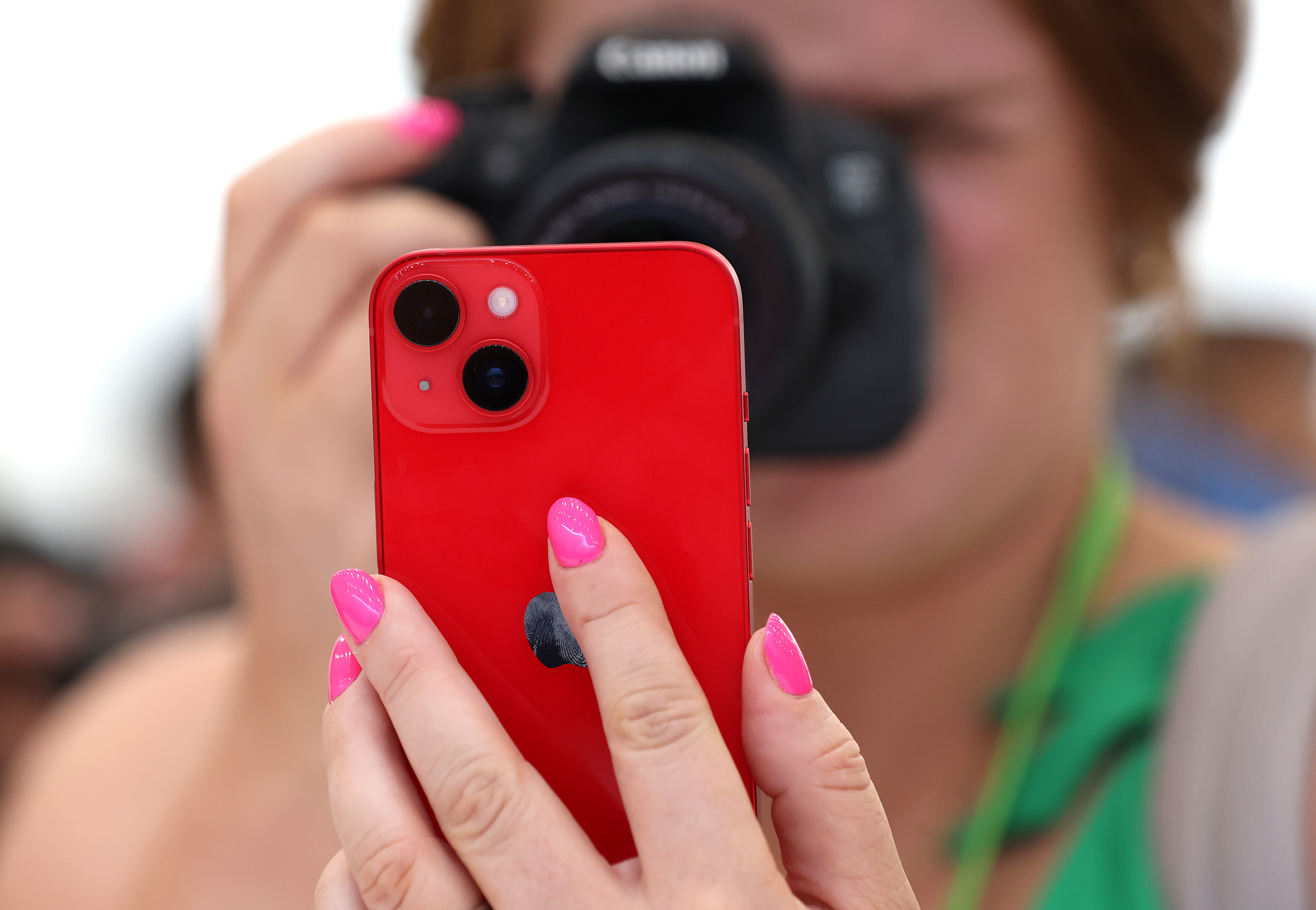 A person holds a traditional camera to their face while holding an iPhone in their hand.