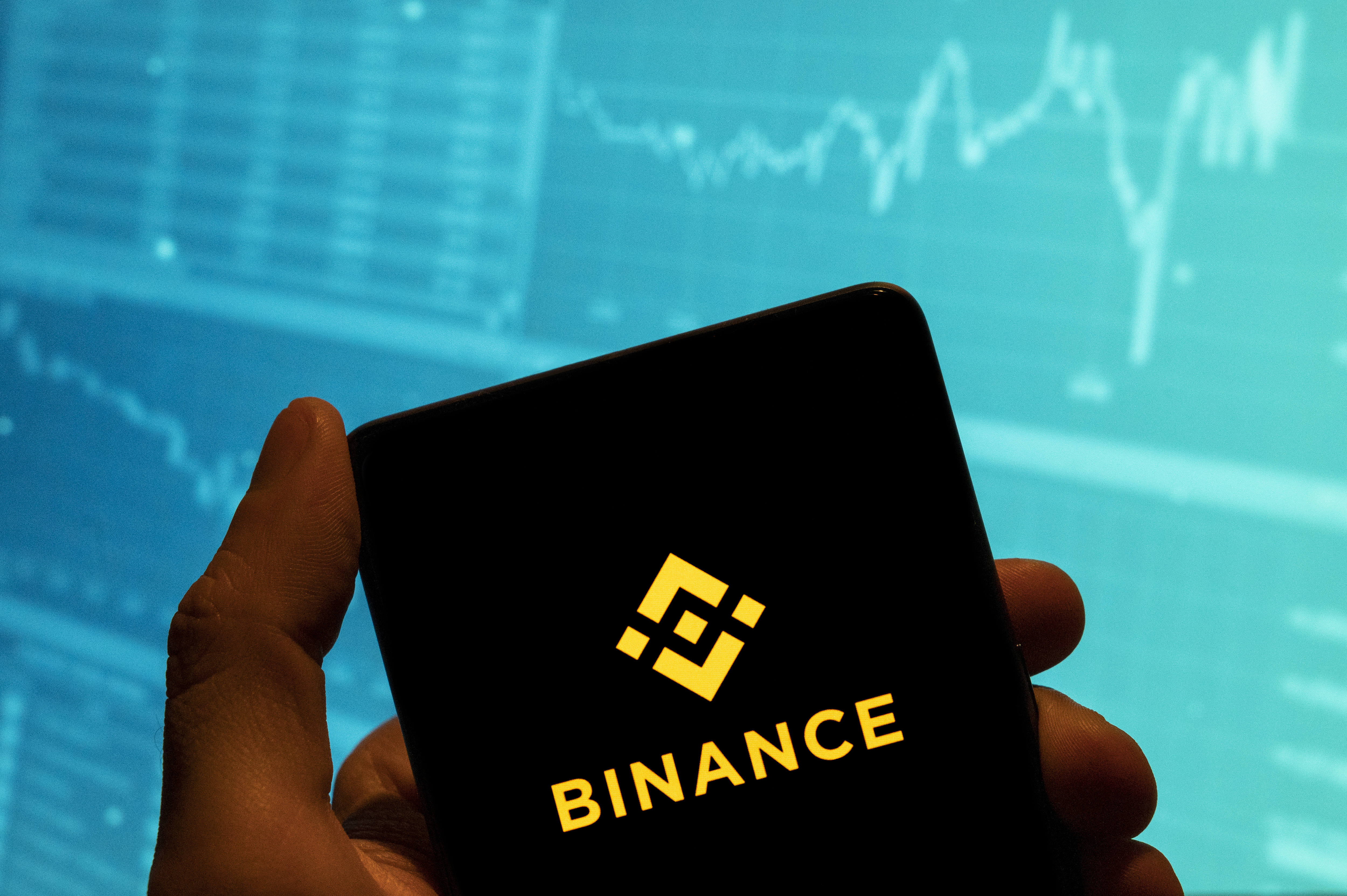 In this photo illustration, the cryptocurrency exchange trading platform Binance logo is seen displayed on a smartphone with an economic stock exchange index graph in the background.