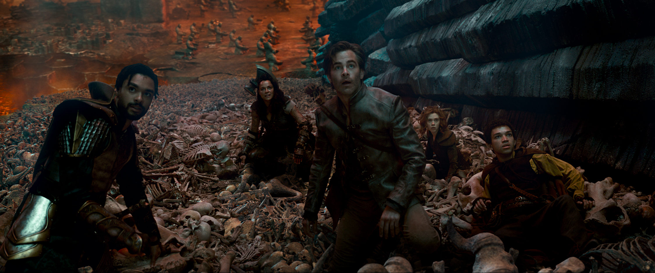 In a still from the movie Dungeons and Dragons: Honor Among Thieves, from left, actors Rege-Jean Page, Michelle Rodriguez, Chris Pine, Sophia Lillis, and Justice Smith in a scene as they climb a hill covered in skeletons and bones.