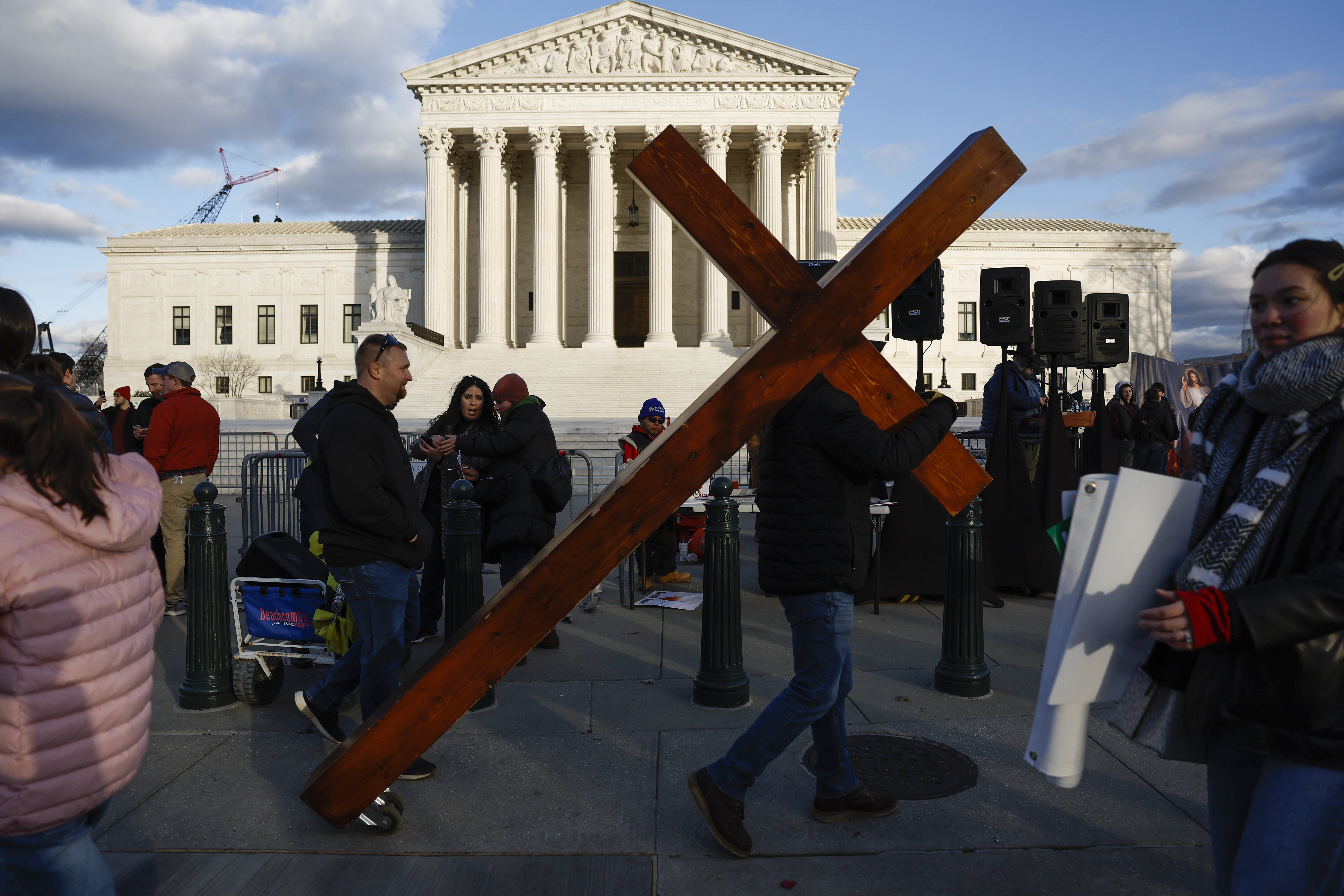 A person carrying a huge Christian cross at a protest in front of the Supreme Court building.
