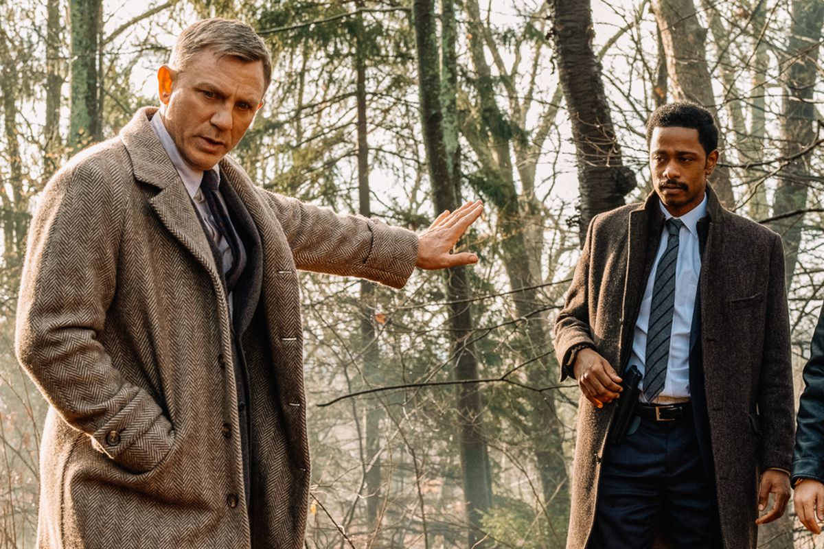 Daniel Craig, Lakeith Stanfield, and Noah Segan stand in the woods in the movie “Knives Out.”