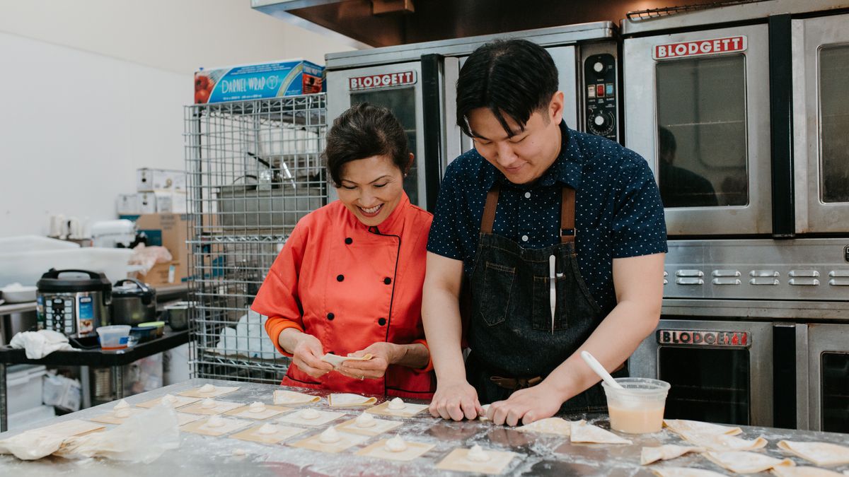 Chef Eric Pham and his mother Khue Pham stand in an industrial kitchen, displaying plates of various Vietnamese dishes.