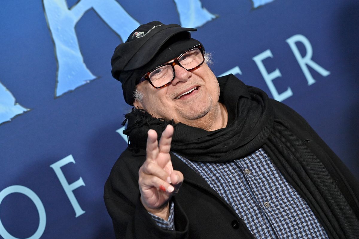 Danny DeVito giving the peace sign on the blue carpet of the premiere of Avatar: Way of Water