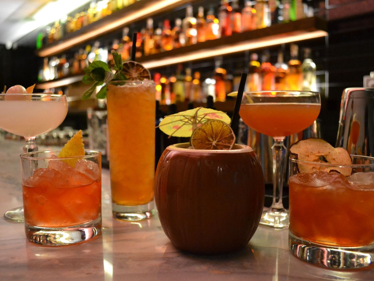 an array of tropical cocktails sitting on a bar, including a drink served in a coconut-shaped mug with a tiny umbrella