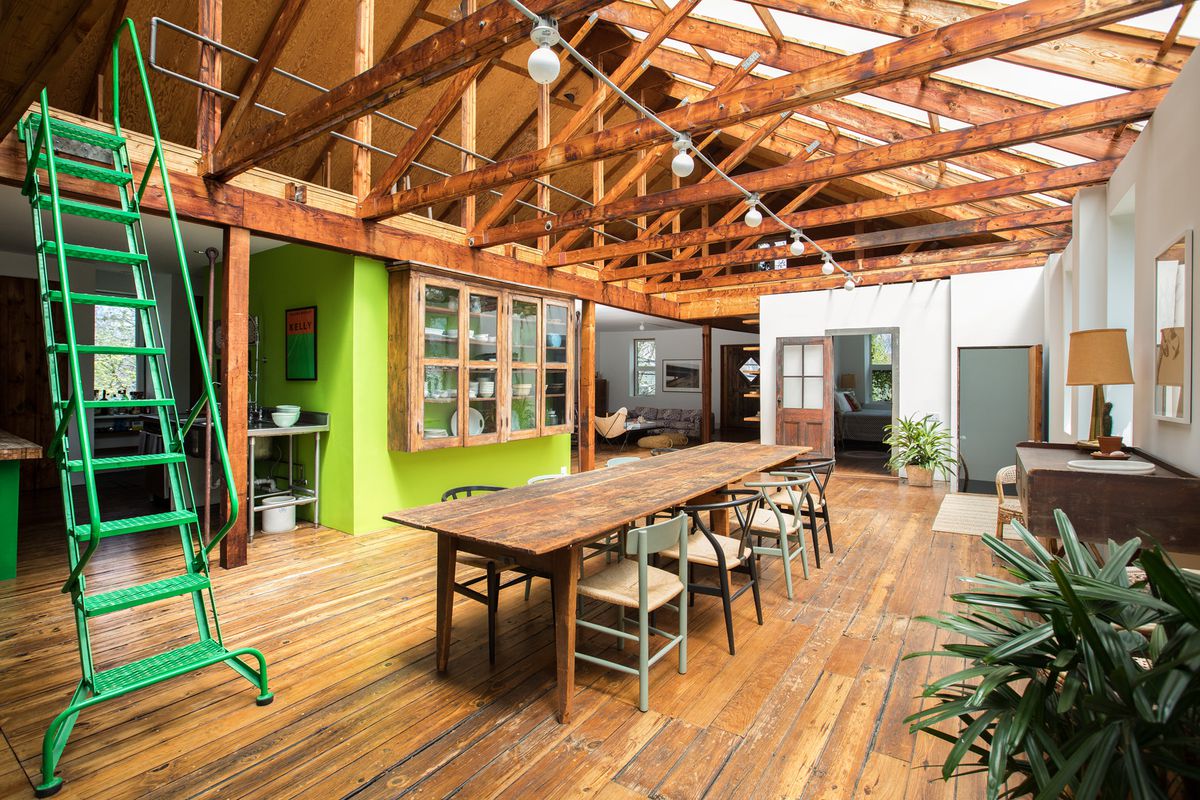 A rafted open living area has a wooden table, wood floors, and a bright green staircase.