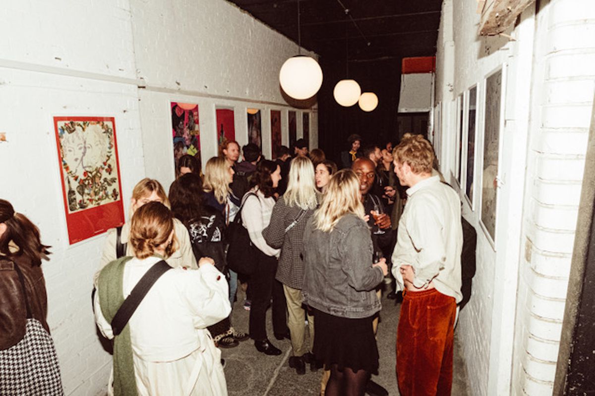 People mingle with wine in a whitewashed gallery space, art on the walls.