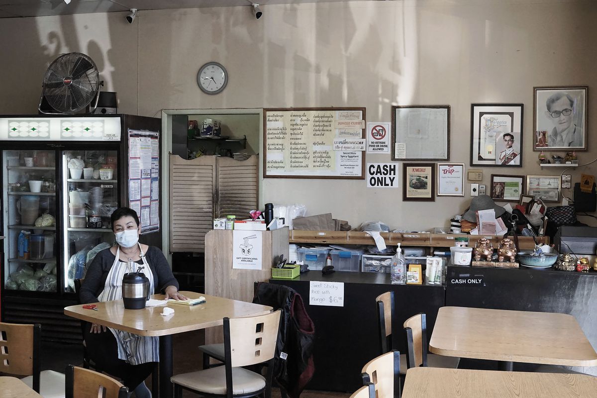 A lone owner sits inside of a restaurant wearing a mask during coronavirus.