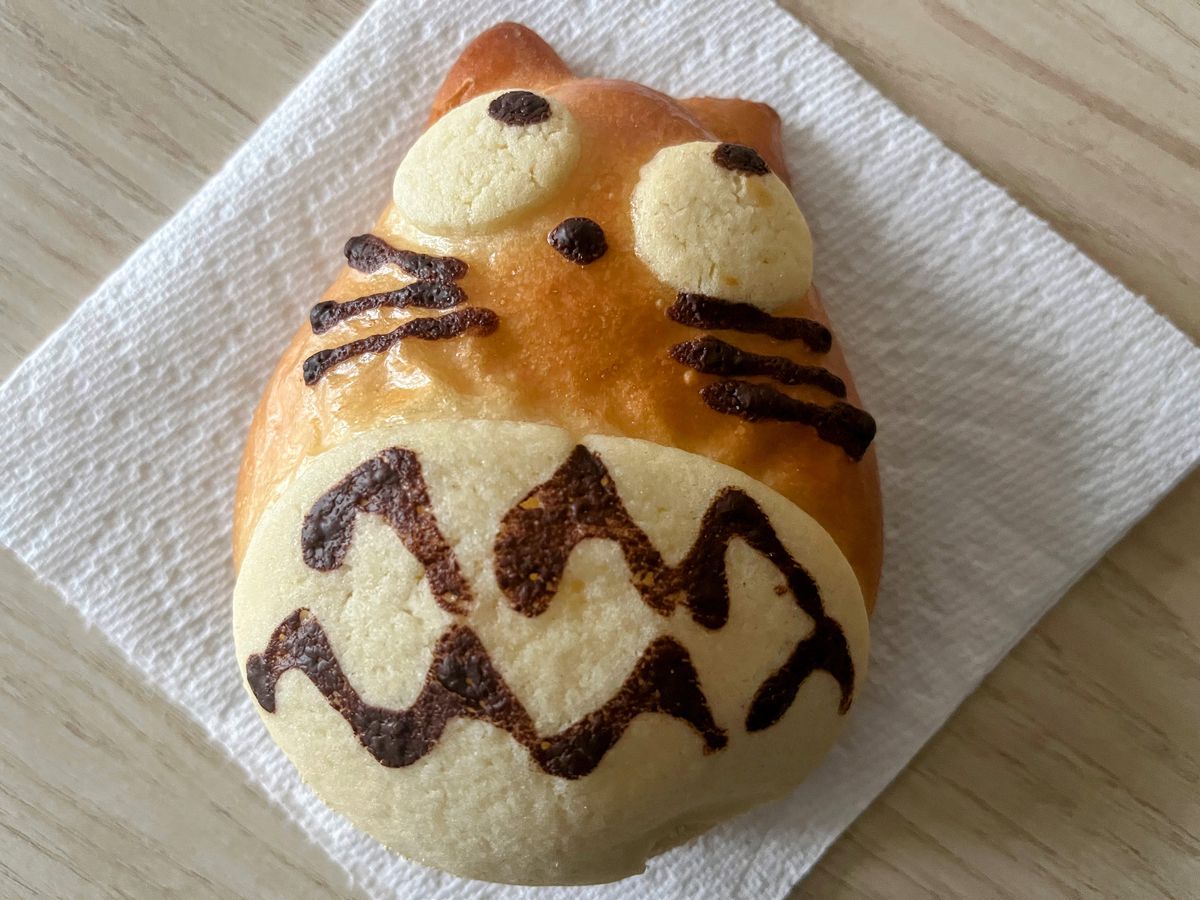 A cream puff shaped like cartoon cat lies on a white paper towel square.