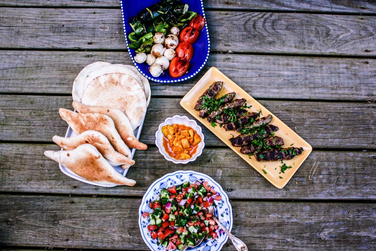Trays of vegetables and pita sit on a wooden table