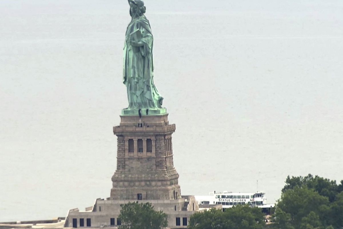 This image taken from video shows people climbing on the side of the Statue of Liberty's pedestal on Wednesday, July 4, 2018 in New York. Several people who hung a banner calling for abolishing Immigration and Customs Enforcement from the statue's pedesta