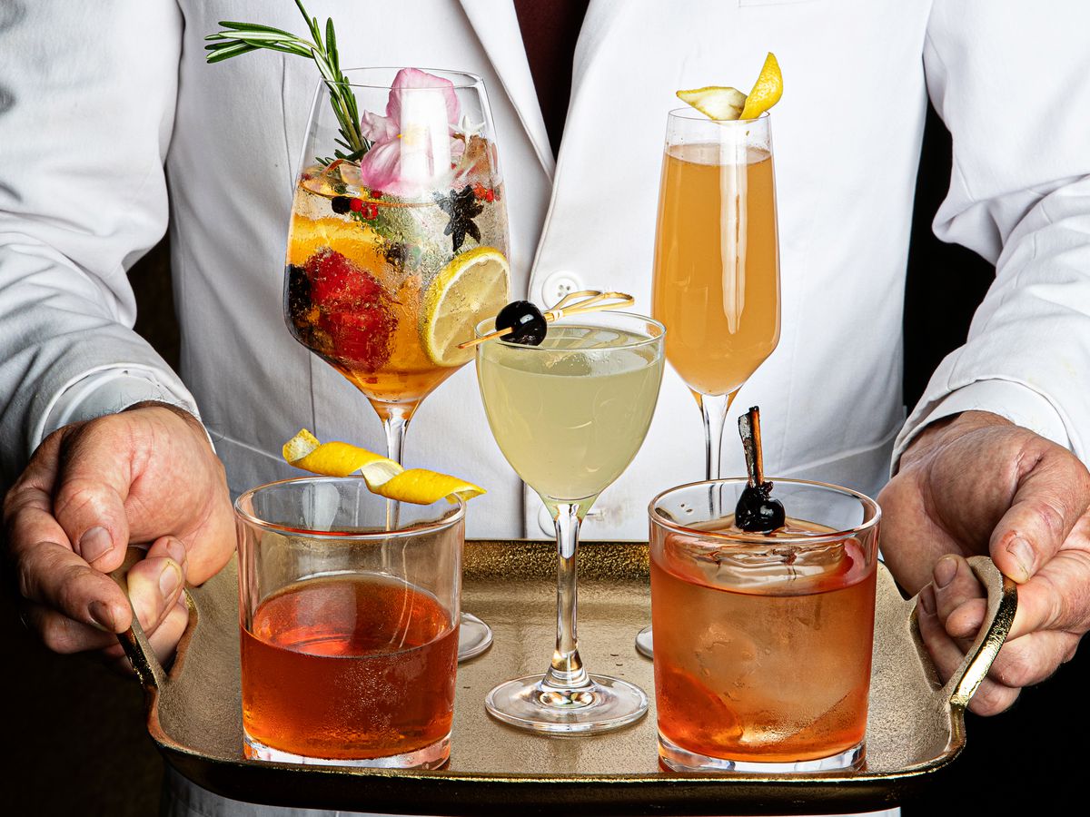 A man holding a tray of fancy cocktails. 