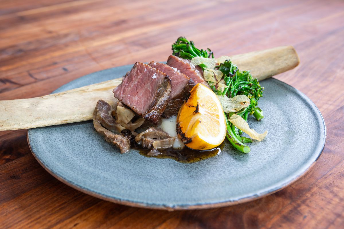 Short rib sliced into thick squares, served with a charred lemon half, broccolini, and a long bone.
