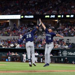 AUGUST 13: Eugenio Suarez #28 of the Seattle Mariners celebrates with third base coach Manny Acta #14 of the Seattle Mariners after hitting a solo home run off of Brock Burke #46 of the Texas Rangers in the top of the sixth inning at Globe Life Field on August 13, 2022 in Arlington, Texas.