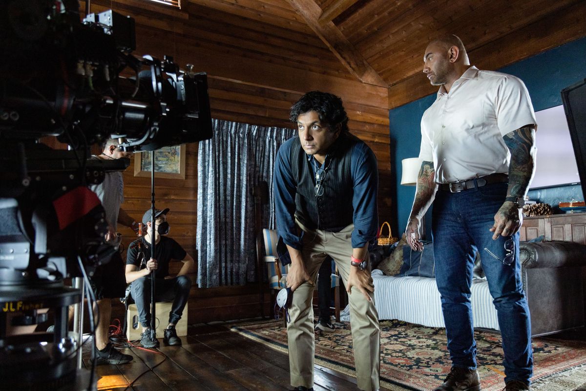 M. Night Shyamalan crouches in front of the camera on the set of Knock at the Cabin with star Dave Bautista.