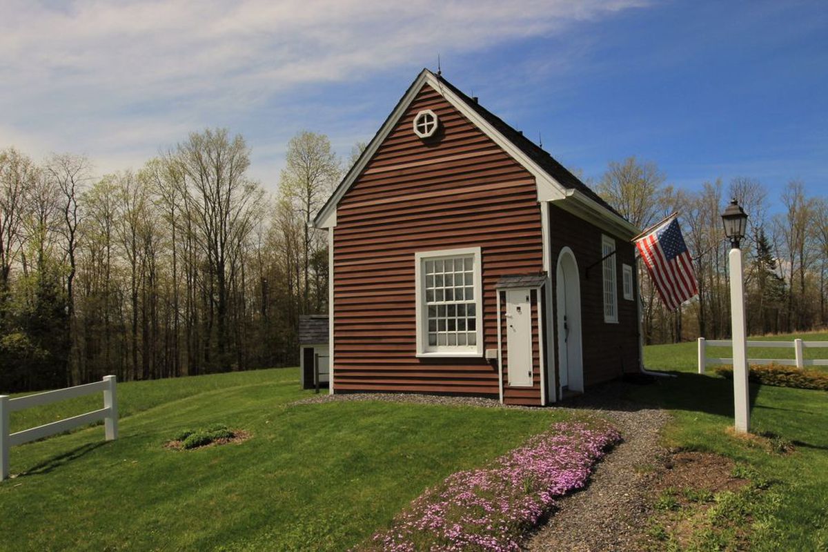 A small shingled cottage with white trim sits on an expansive plot of rolling hills. 