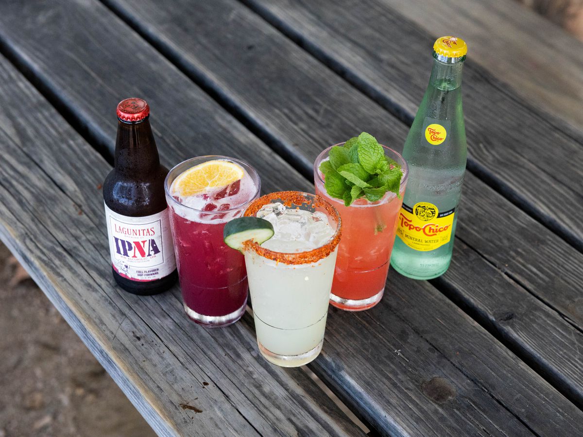 A lineup of non-alcohol drinks, including a Topo Chico, a Lagunitas IPNA, and garnished cocktails.
