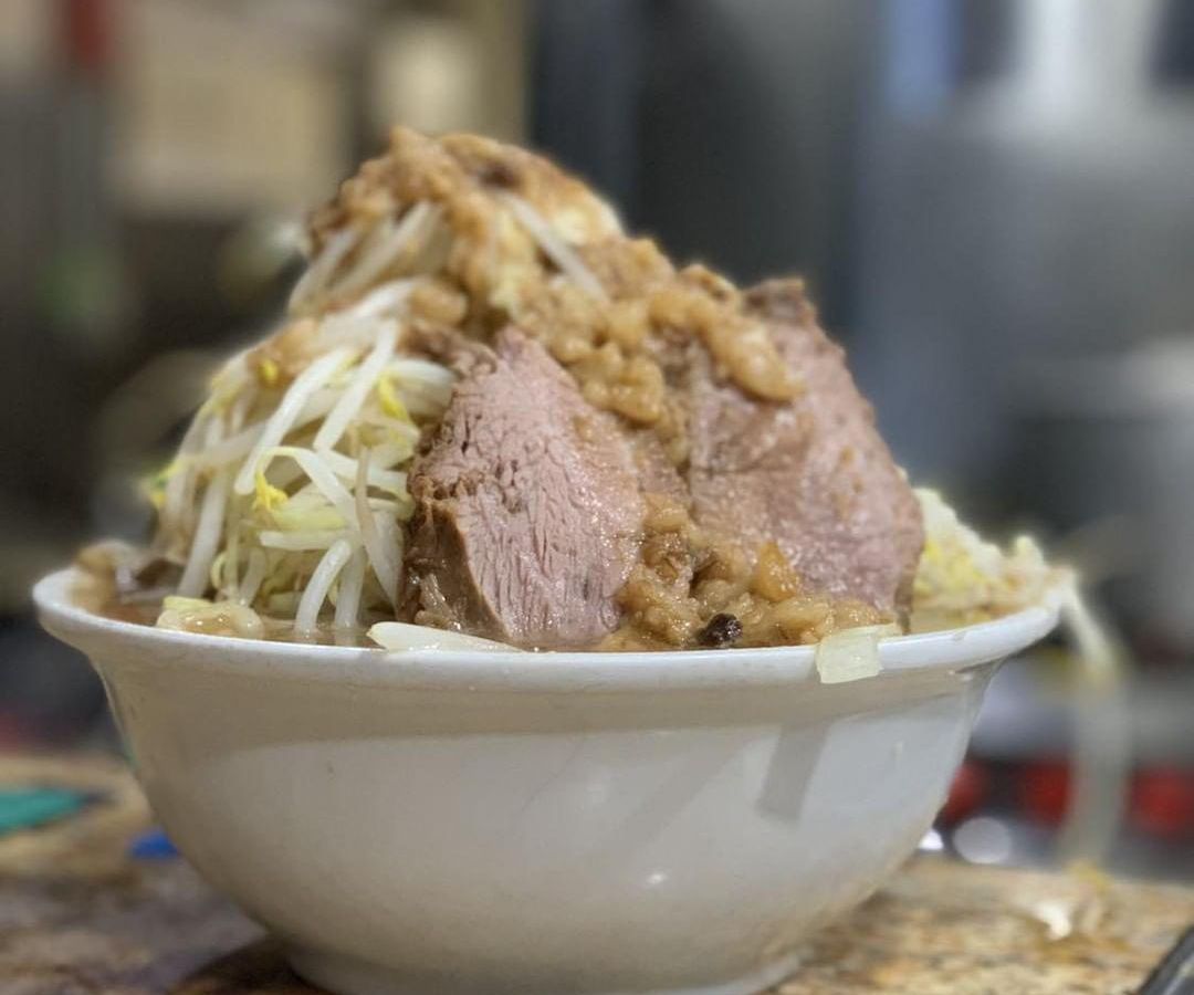 Ramen noodles and slices of pork are stacked impossibly high in a white bowl, topped with ample garlic.