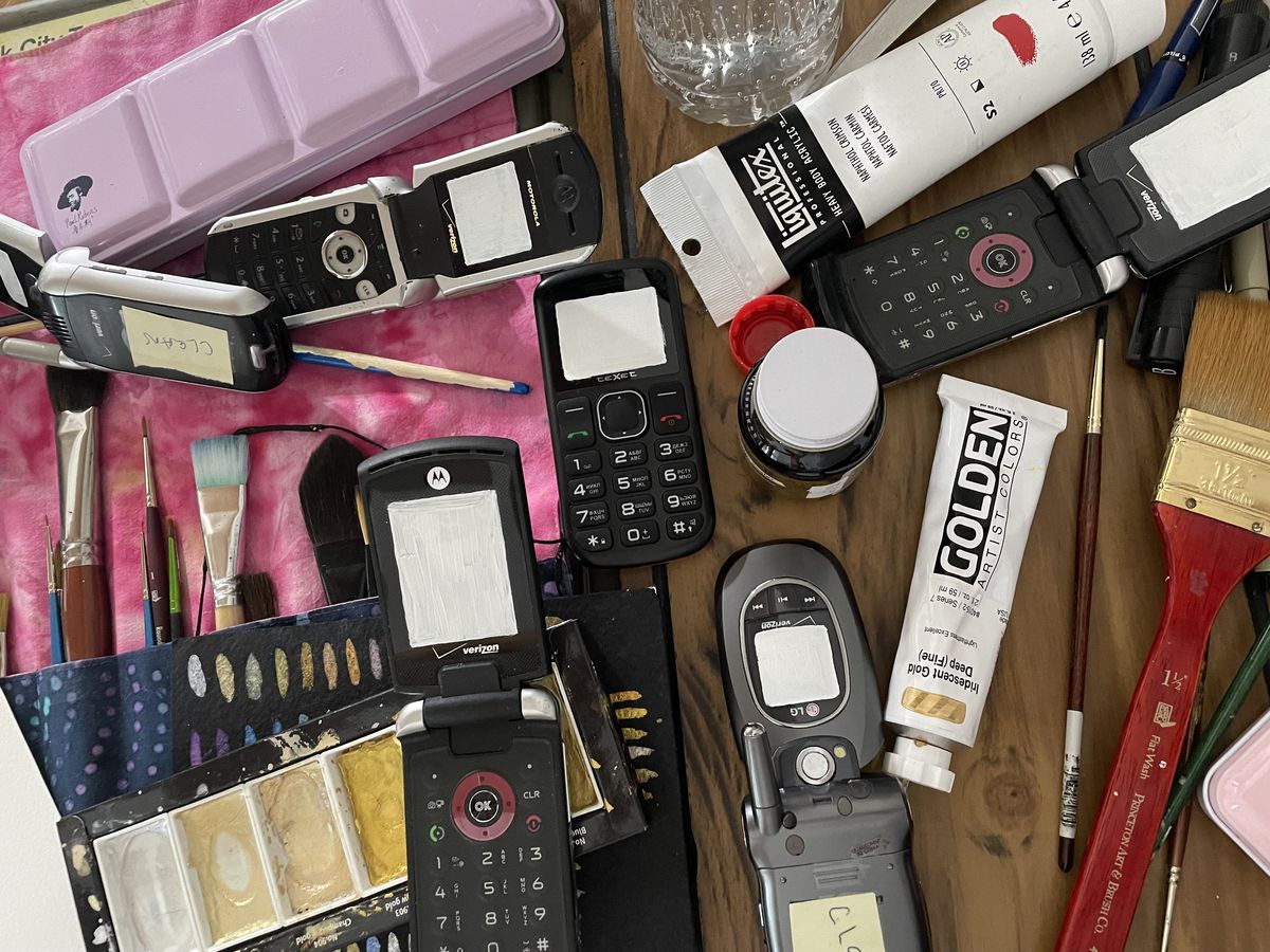 A photograph of paintbrushes and several old cell phones