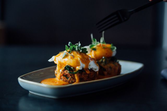 Two croquettes topped with poached eggs and an orange sauce on a gray, rectangular plate.