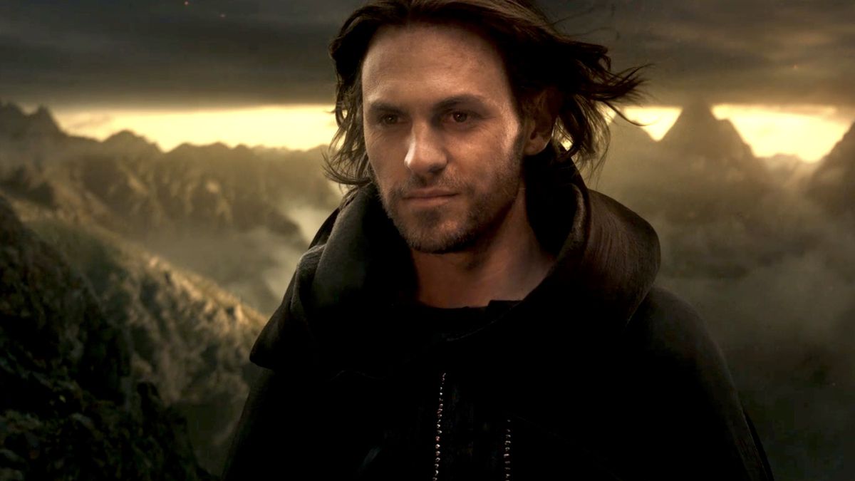 Charlie Vickers’ Sauron in full runway model mode, hair blowing in the wind as he struts up to Mount Doom wearing a black cloak in The Lord of the Rings: The Rings of Power