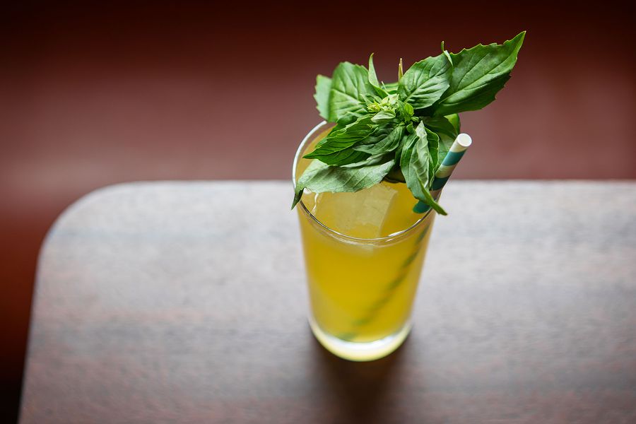 A yellow beverage in a tall glass with mint garnich and paper straw.