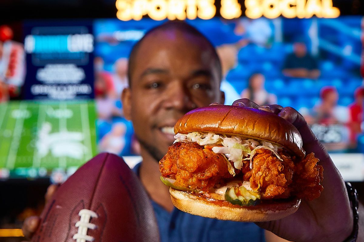 A man holding a football and a chicken sandwich.