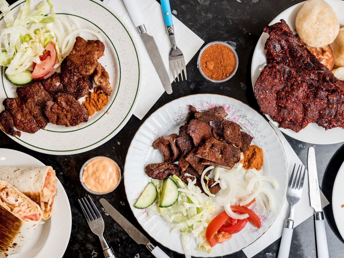 A spread of Hausa suya, grilled beef spiced with yaji, served on white plates with a salad of lettuce, tomato, and raw onion.