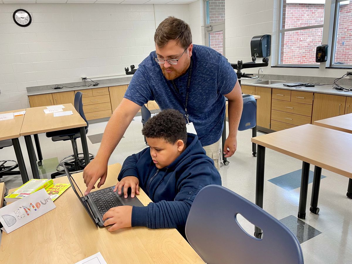 A teacher works with his student, who is working on a computer in the classroom.