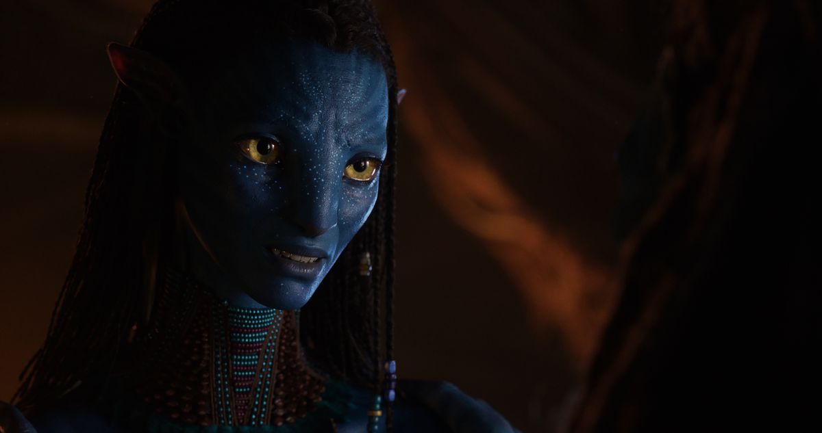 Na’vi protagonist Neytiri (Zoe Saldaña) sits in a dark space smiles at someone offscreen in a scene from Avatar: The Way of Water