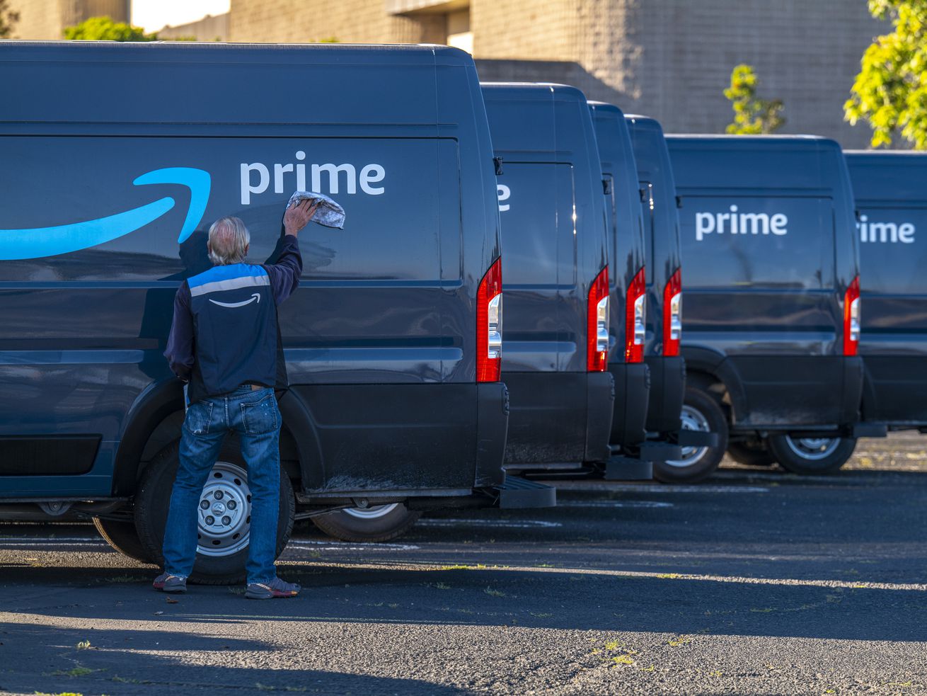 A contractor cleans the word “prime” on an Amazon delivery truck in California. The truck is one of several parked in a row.