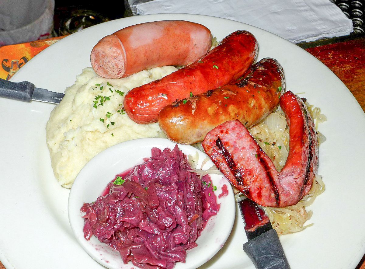 A white plate with mashed potatoes, several sausages, and a smaller plate with red cabbage.