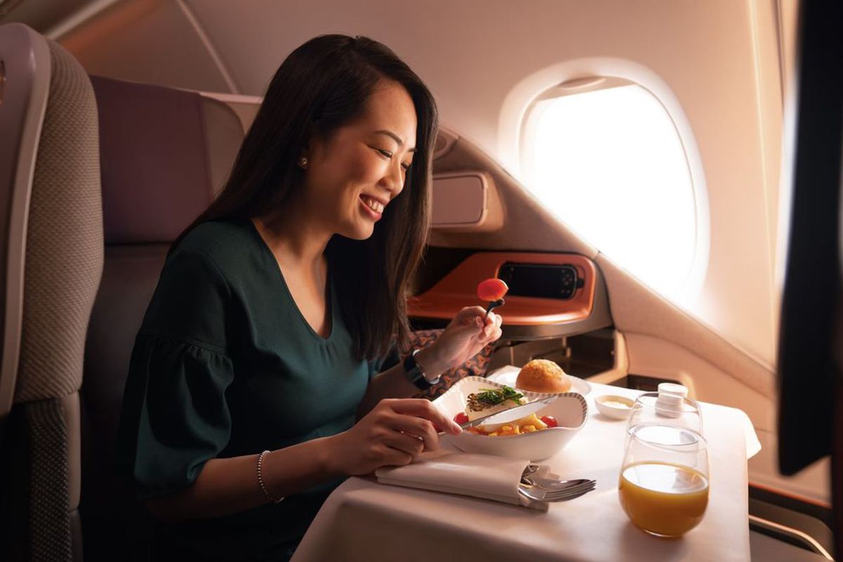 Woman seated on an airplane eating a luxury meal.