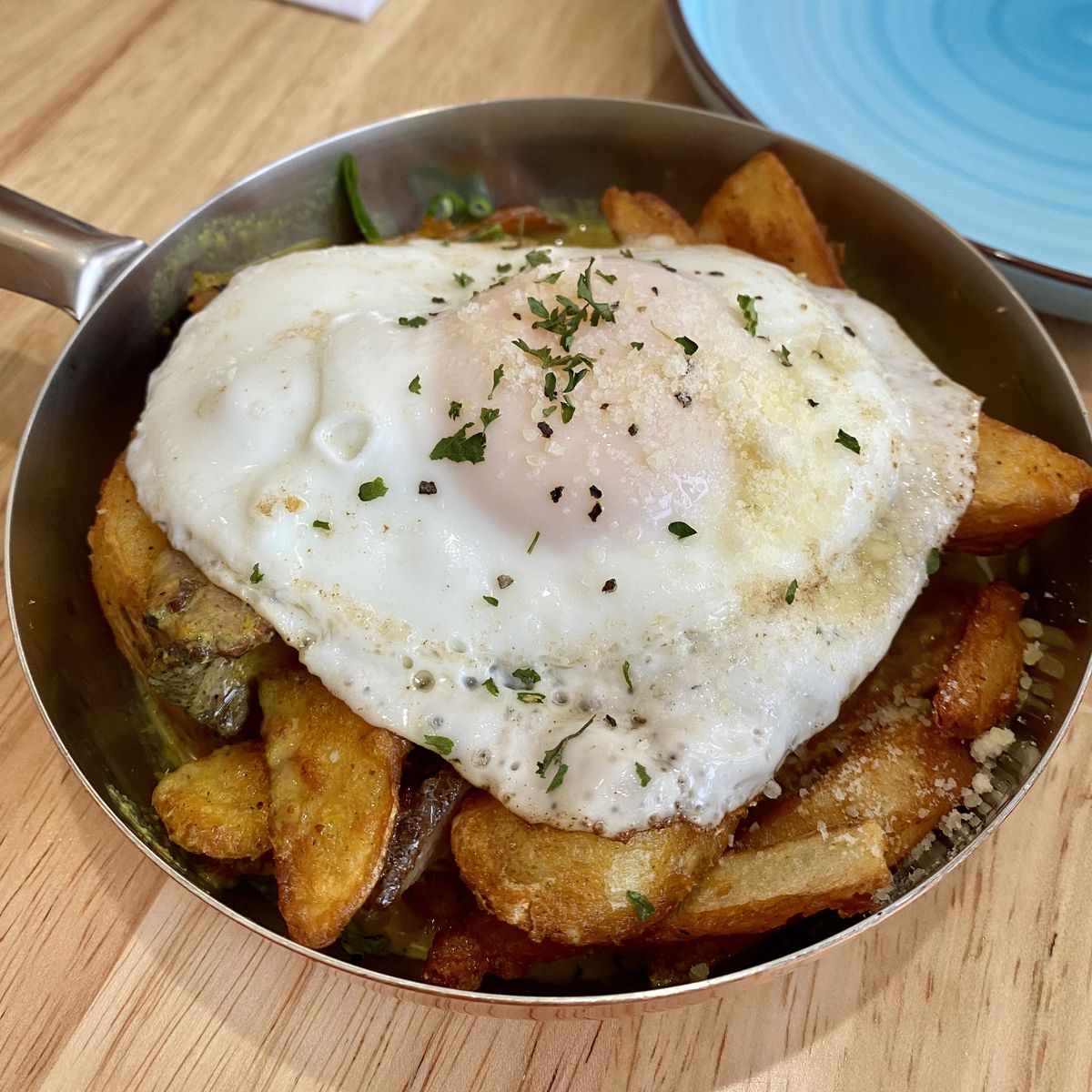 A small pan of potatoes topped with an overeasy egg.