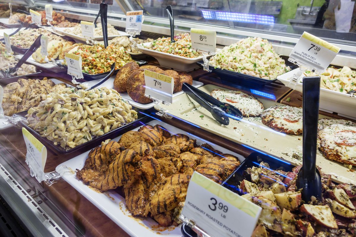 Grilled meats and potato salads behind a glass deli counter in a Publix.