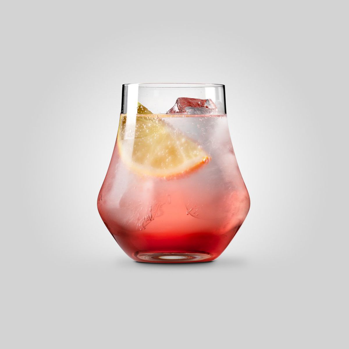 A red-colored drink in a glass with ice and lemon