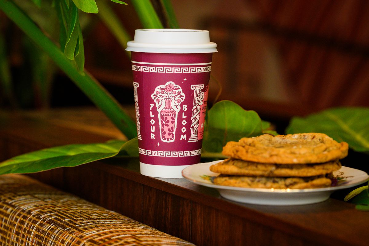 A coffee cup sits next to a plate of cookies at Flour Bloom.