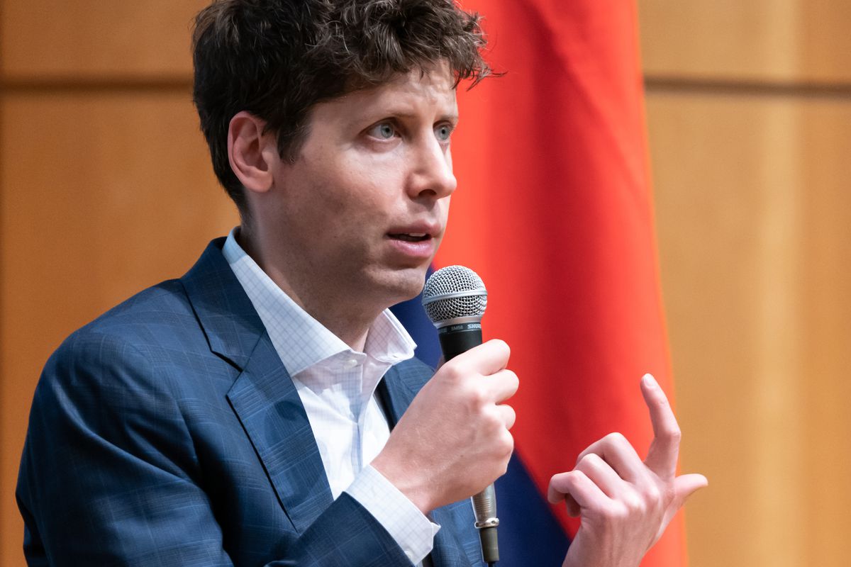 Sam Altman, a white man with curly brown hair wearing a blue suit and white shirt, speaks into a microphone to an unseen audience.
