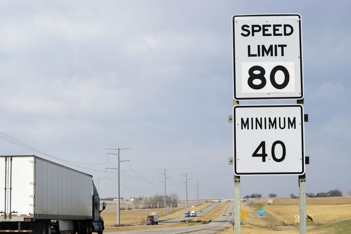A photo of a trailer truck on a long flat highway passing a sign showing a speed limit minimum of 40 m.p.h. and maximum of 80 m.p.h.