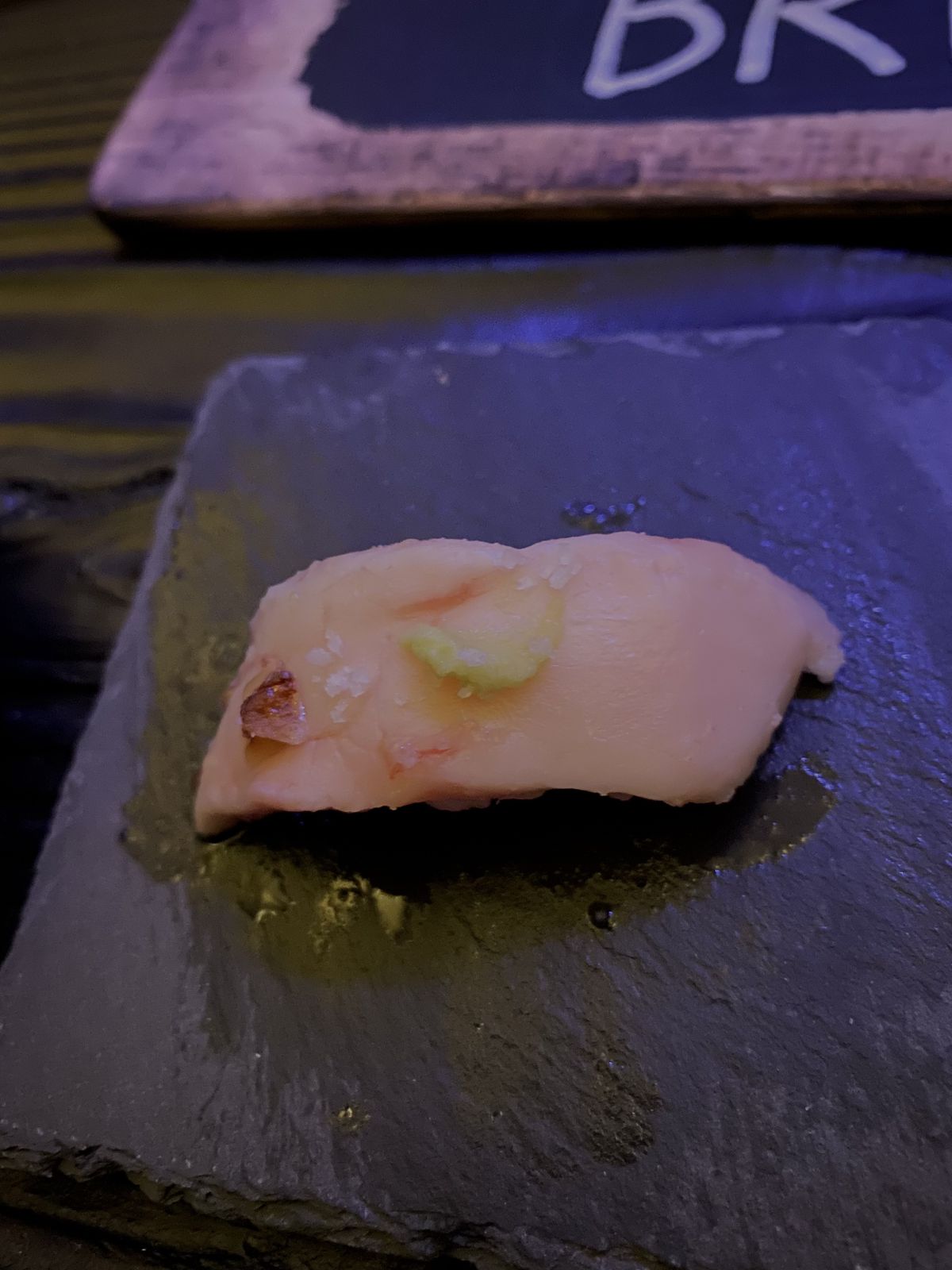 A piece of white bone marrow nigiri on a piece of slate.